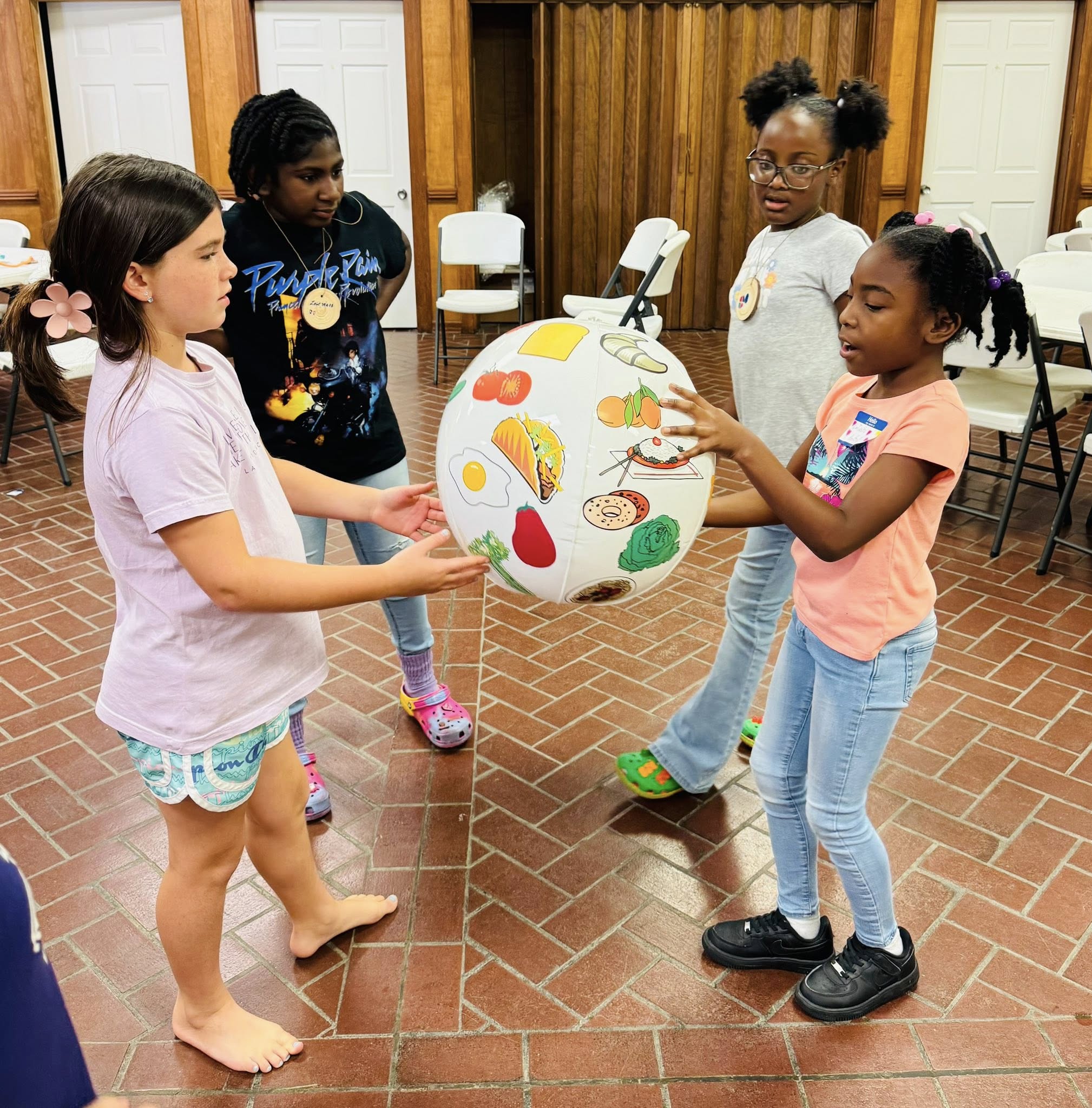 Four girls playing with a ball that has pictures of different foods on it.